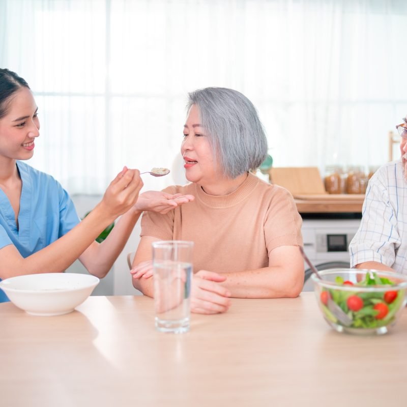 nurse-or-doctor-who-work-as-homecare-staff-help-to-serve-a-spoon-of-mush-rice-to-senior-woman.jpg